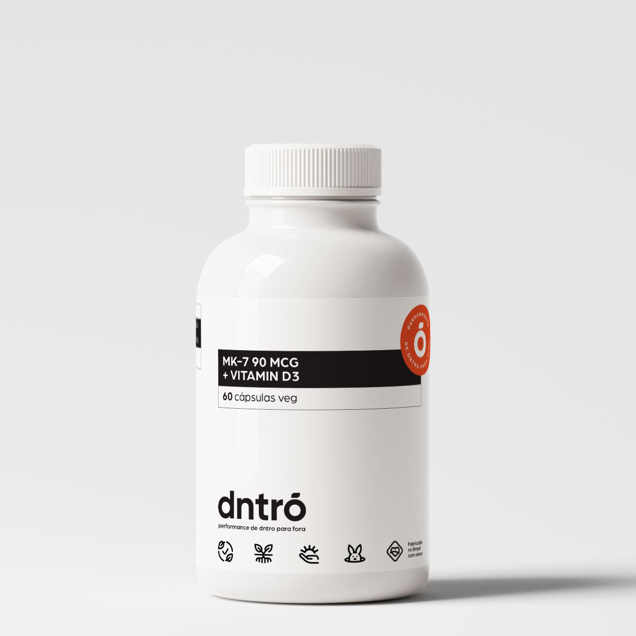 Frasco branco do suplemento DNTRO MK-7 90 mcg + Vitamina D3 com 60 cápsulas veganas. Embalagem minimalista com selo laranja “Performance de dentro para fora” e ícones que indicam produto vegano, sem glúten, sem lactose, cruelty-free e com ingredientes naturais. Suplemento indicado para saúde óssea, cardiovascular e equilíbrio dos níveis de cálcio.