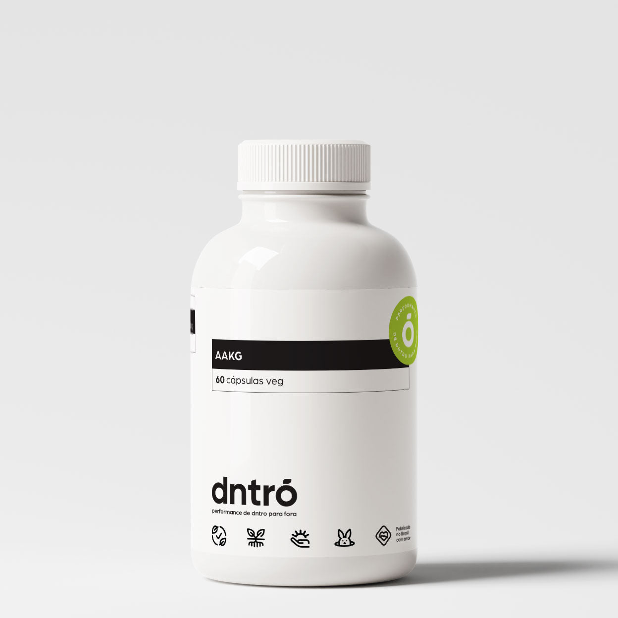 Frasco branco de suplemento alimentar da marca "Dntrō", com o rótulo destacando o nome "AAKG" e a quantidade de "60 cápsulas veg". O design é minimalista, com elementos gráficos que indicam ser um produto vegano, sem glúten, sem lactose e não testado em animais. Há um selo verde destacando o uso de ingredientes naturais. A embalagem transmite uma proposta de saúde, performance e bem-estar.