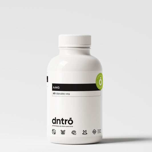 Frasco branco de suplemento alimentar da marca "Dntrō", com o rótulo destacando o nome "AAKG" e a quantidade de "60 cápsulas veg". O design é minimalista, com elementos gráficos que indicam ser um produto vegano, sem glúten, sem lactose e não testado em animais. Há um selo verde destacando o uso de ingredientes naturais. A embalagem transmite uma proposta de saúde, performance e bem-estar.